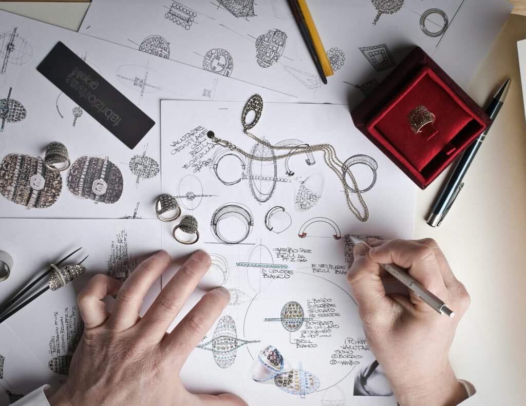 Inspiration Gallery Hands sketching jewelry designs with tools and prototypes on a desk.
